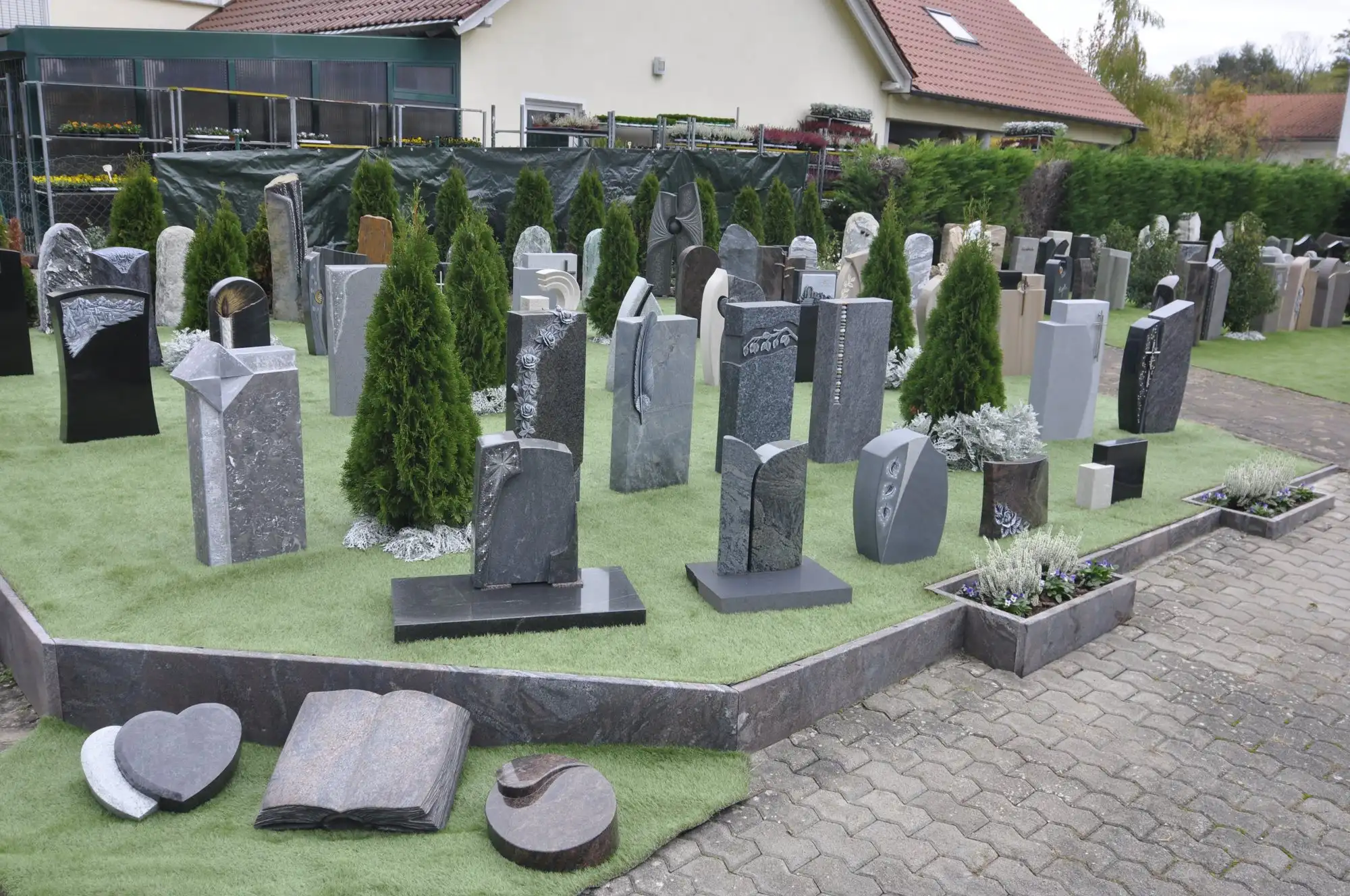 Freigelände der Grabmalausstellung: viele Grabsteine auf Rasen zwischen kleinen Koniferen