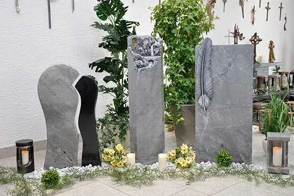Grabsteine mit Feder- und Felsrelief zwischen Pflanzen und Grablaternen
