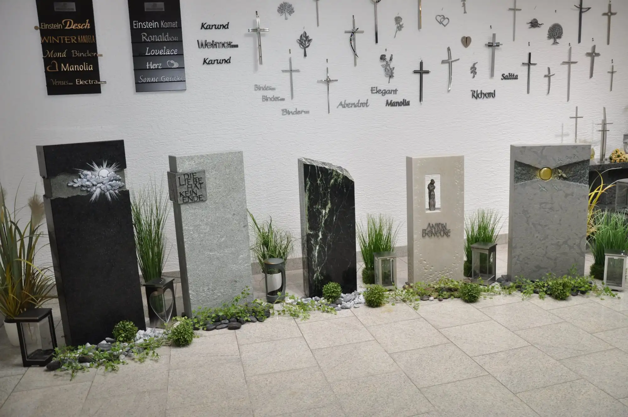 Grabsteine im Ausstellungsraum, darüber Schriftmuster und Kreuze an der Wand