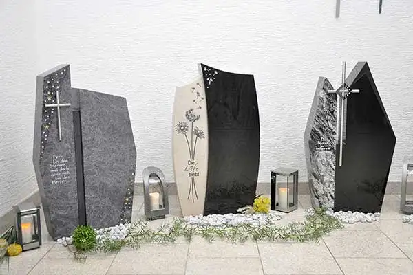 Grabsteine mit Metallkreuzen und glitzernden Einsätzen, ein heller Stein mit Pusteblumen-Motiv